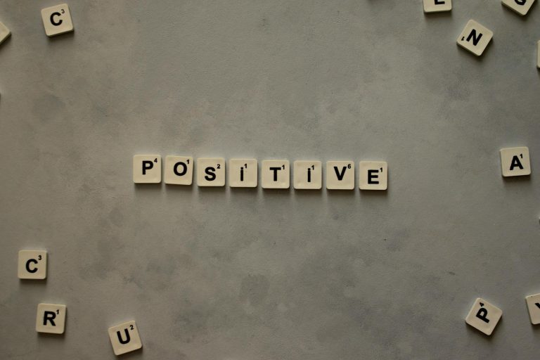 Scrabble tiles arranged to spell 'positive' on a gray textured surface, conveying optimism.
